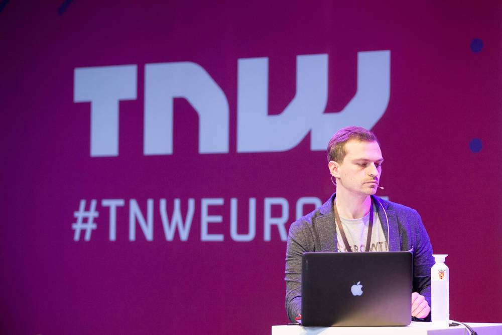A speaker sits behind a laptop on stage in front of a large '#TNWEUROPE' logo.