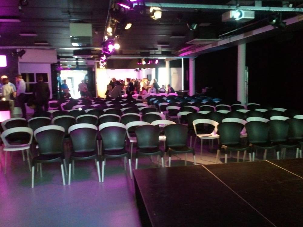 An empty purple-lit event hall set up with rows of chairs for a presentation.