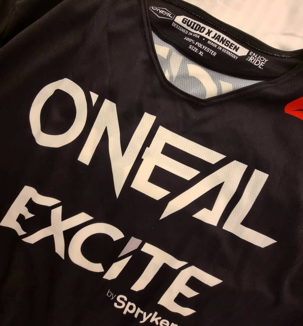 Close-up of a black O'Neal Excite by Spryker jersey, its collar tag printed with the name Guido X Jansen.