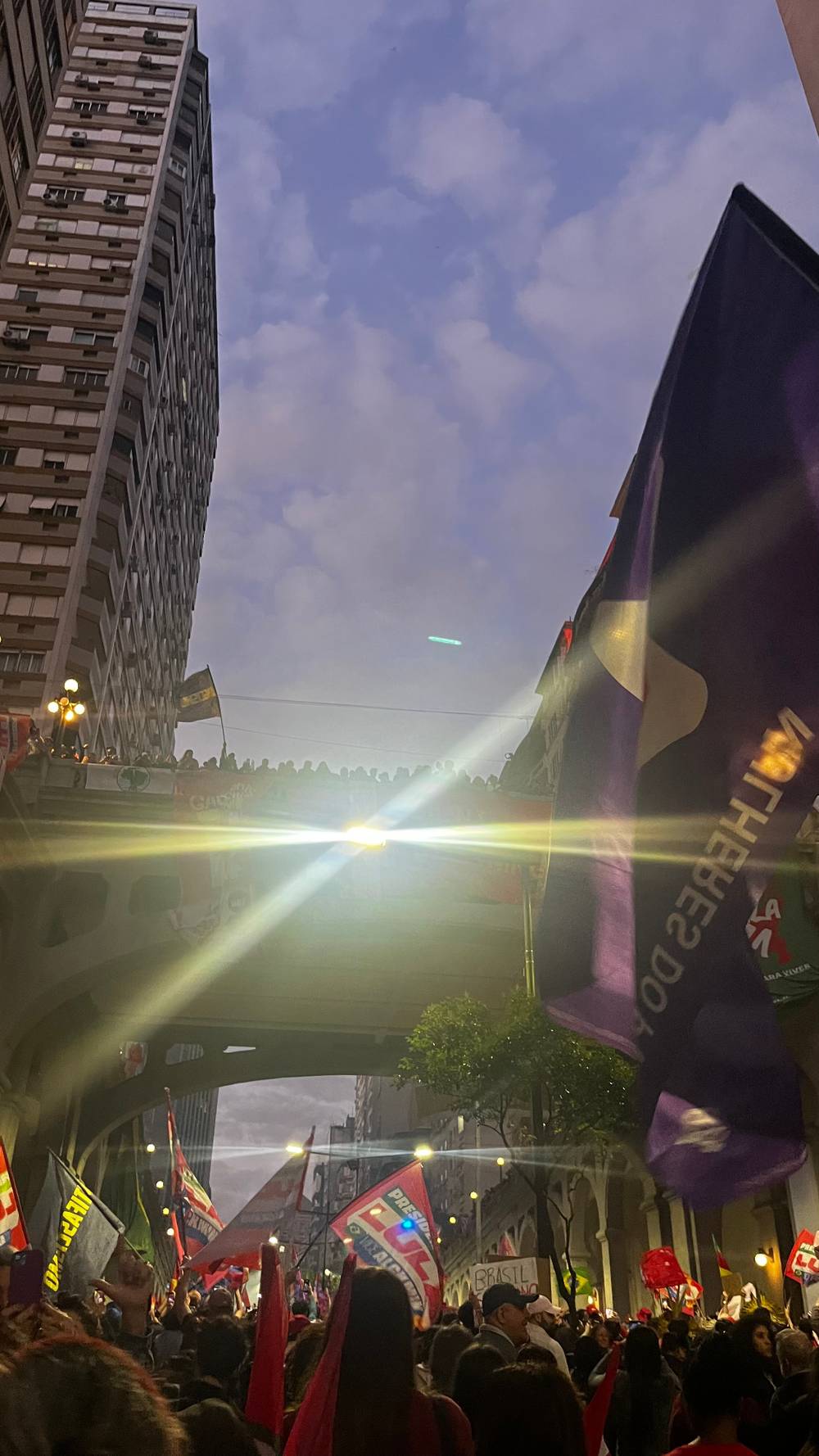 O viaduto Otávio Rocha, visto de baixo, tomado de pessoas no entardecer. O reflexo de uma luz bem no meio do viaduto tapa os cartazes que diziam "O Brasil não cabe no quintal de ninguém".