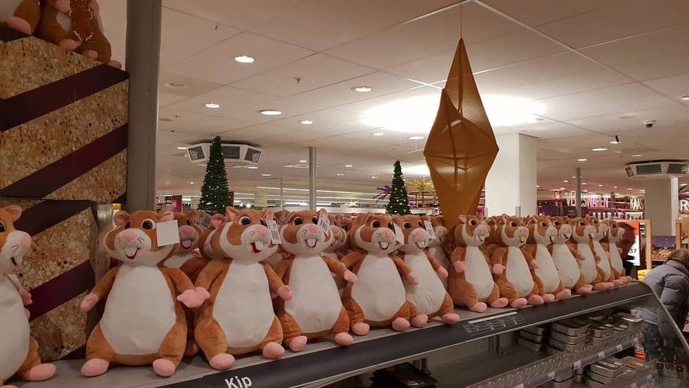 A row of hamster-shaped plush toys lined up on a store shelf beside a gold ornament.
