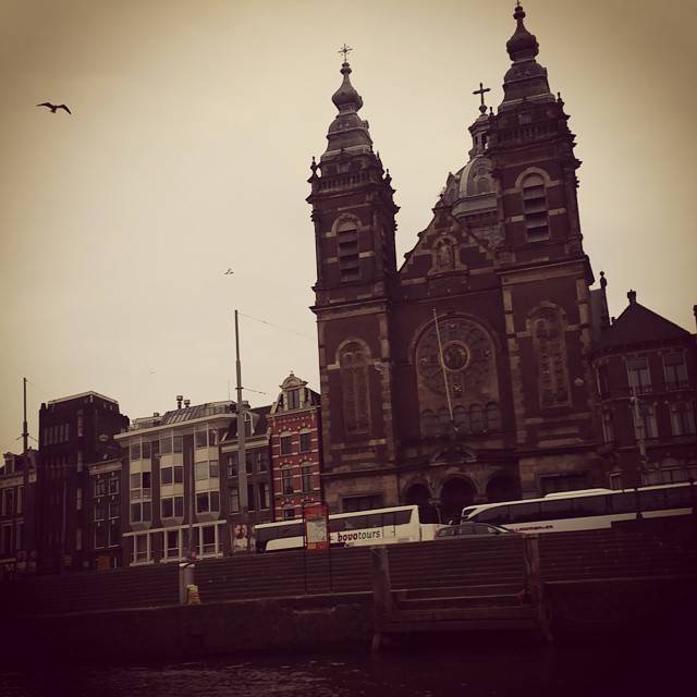 A large brick church with twin spires seen from across a canal.