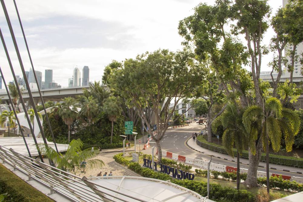 Trees line a road near the Singapore Flyer, with the F1 pit building visible ahead.