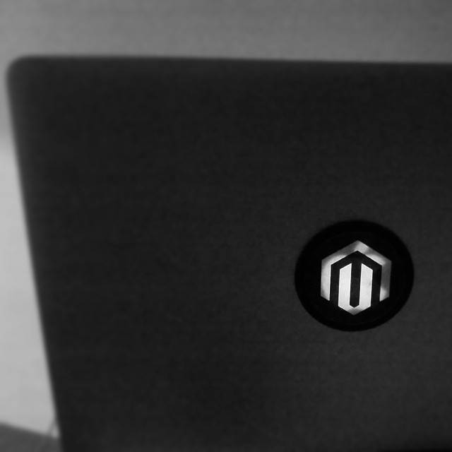 A closed dark laptop with a Magento logo sticker on the lid.