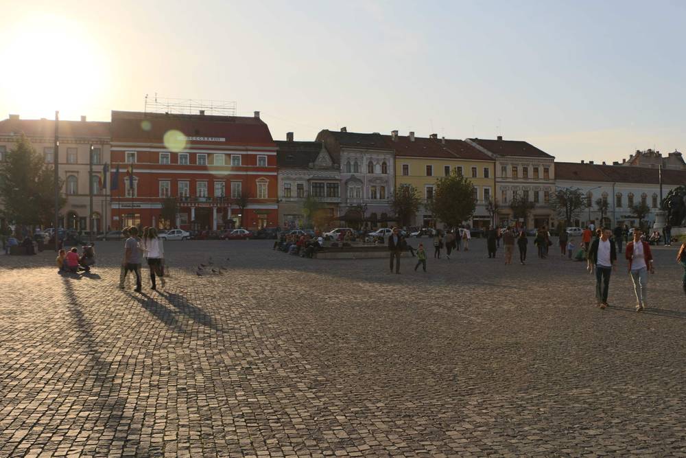 People walking across the same cobblestone square as the low sun casts long shadows.
