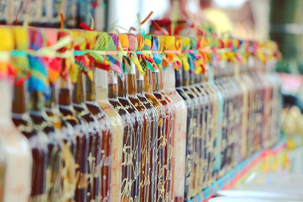 Rows of rum bottles decorated with colourful ribbons at a market stall.