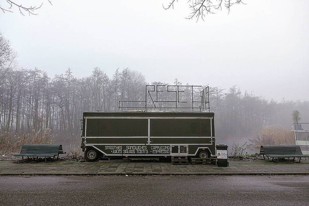 A food truck parked in a foggy park beside empty benches.