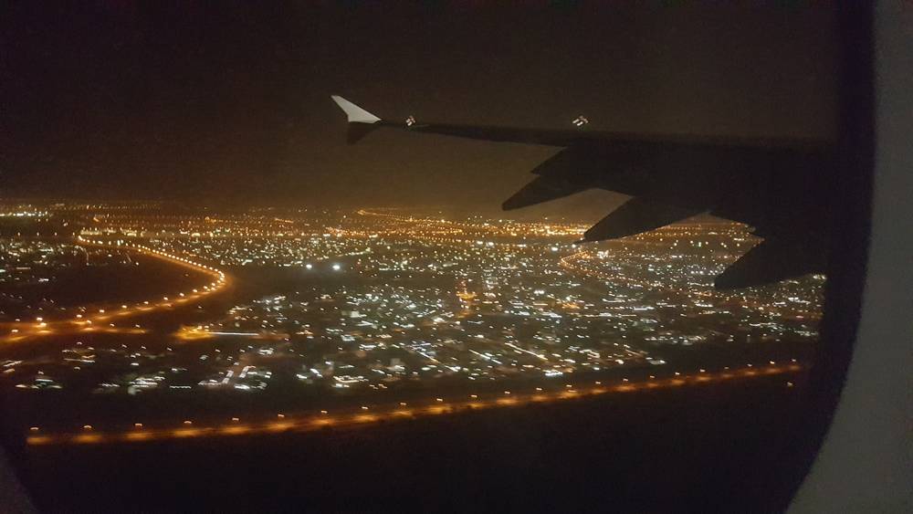 The wingtip and runway lights are visible as the plane descends over a lit-up city at night.
