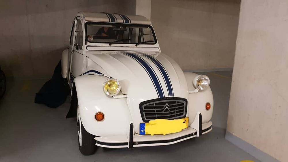 A white vintage Citroen 2CV with blue racing stripes parked in a garage.