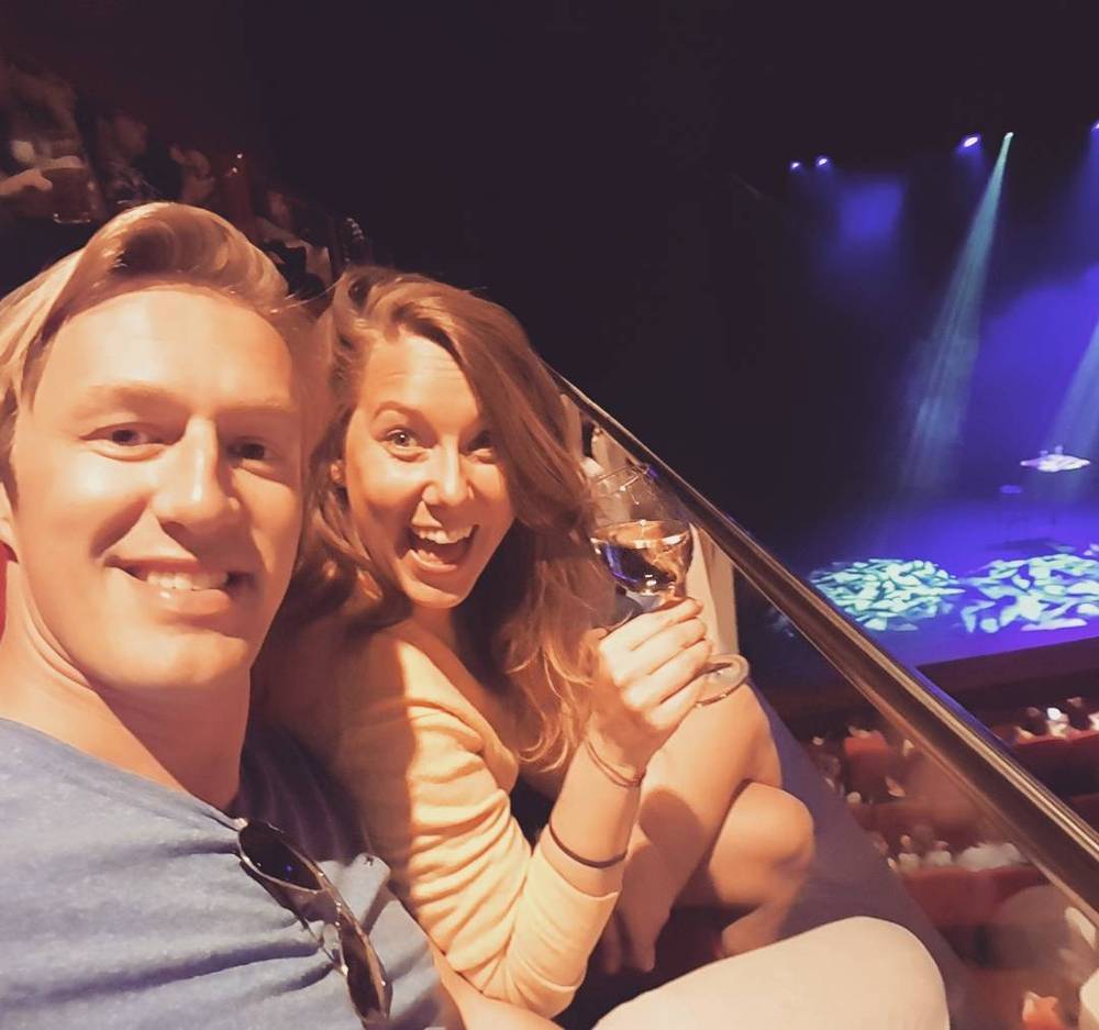 A couple smiling together at a concert, with colorful stage lights in the background.