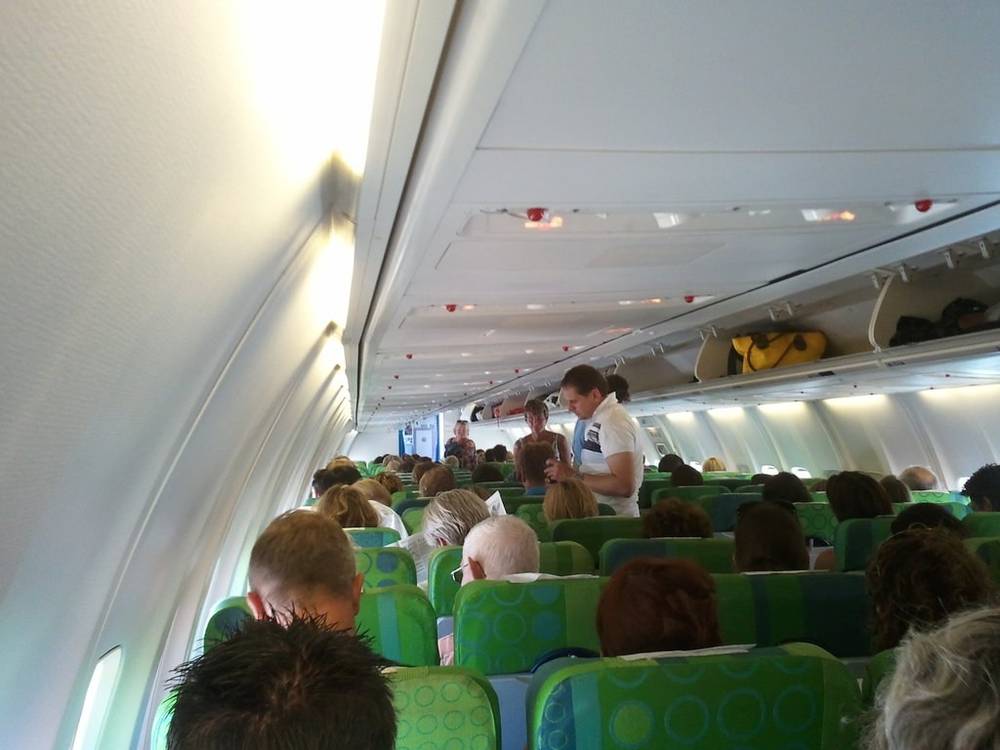 Passengers board a plane while a flight attendant stands in the aisle.