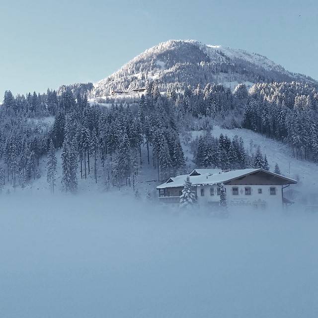 A snow-covered mountain rises above a misty alpine village with a large chalet.