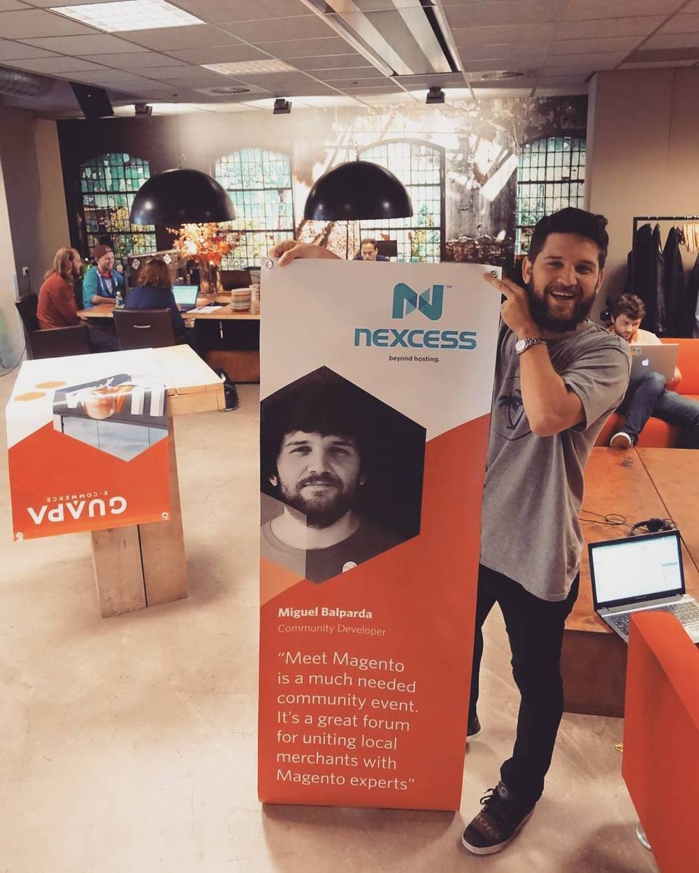 A man poses beside a conference vendor stand with a quote about the Meet Magento community event.