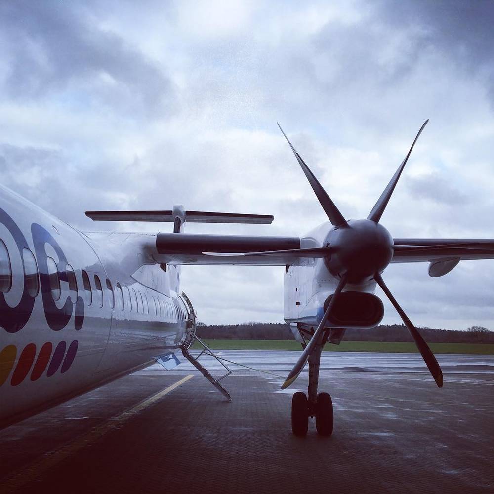 The propeller and nose of a turboprop plane on a wet airport tarmac.
