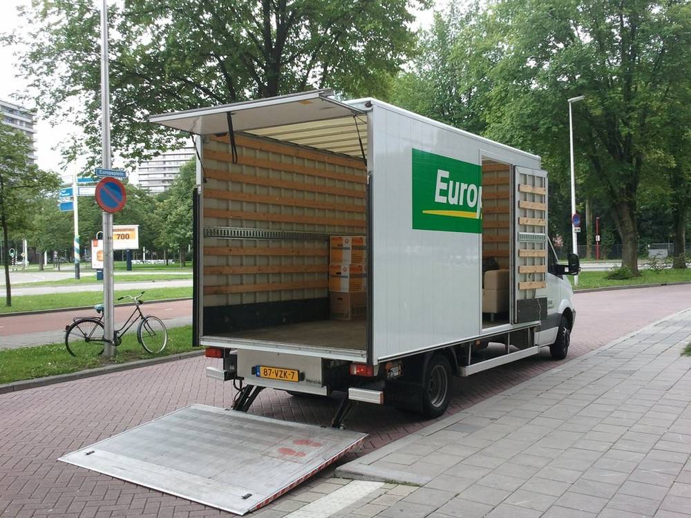 A moving truck with its ramp lowered is parked along a tree-lined street.