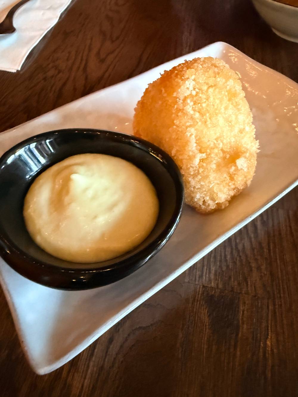 Cheesy Onigiri

A black bowl of yellow sauce and a golden fried food item on a white plate. The plate is on a wooden table.