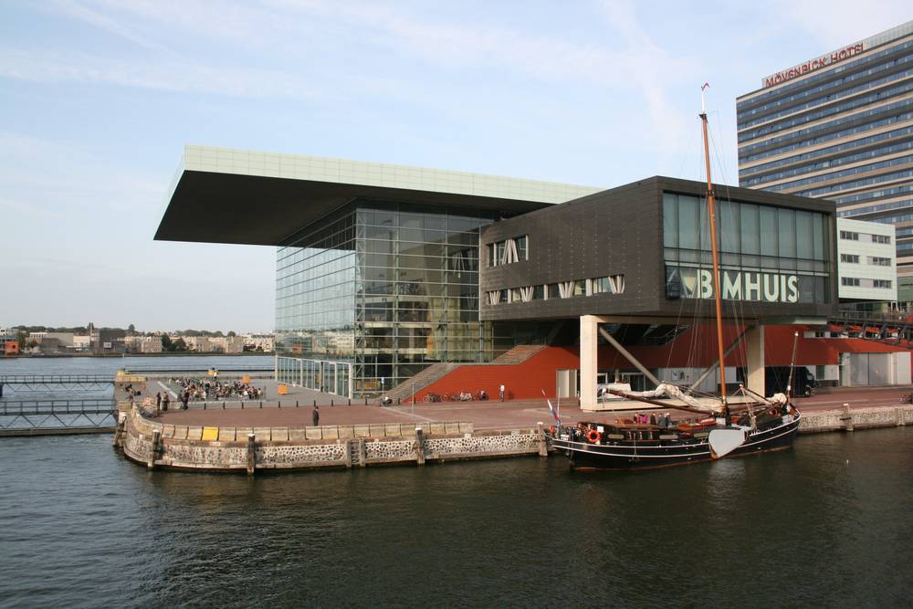 The angular glass Muziekgebouw aan 't IJ concert hall on the Amsterdam waterfront, with a traditional sailing barge moored alongside.