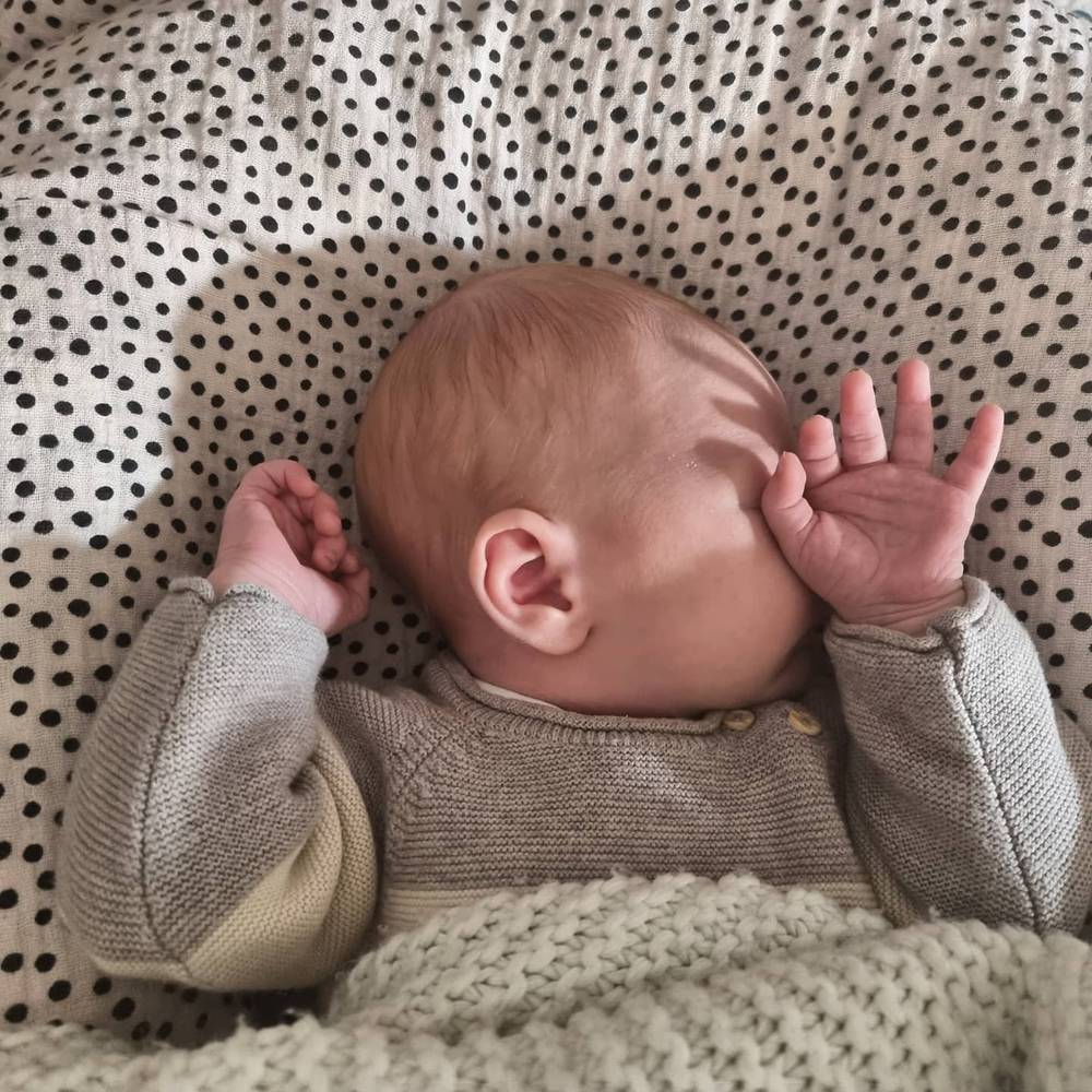 A newborn baby rubbing its eyes while lying on a polka-dot blanket.