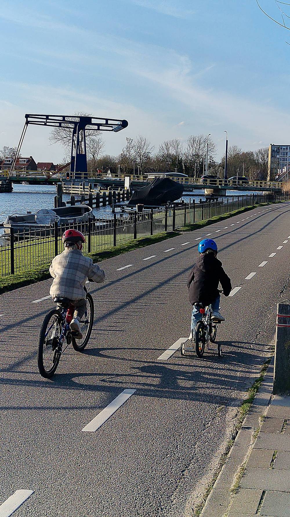A child rides a bike along a canal-side path with another cyclist ahead.