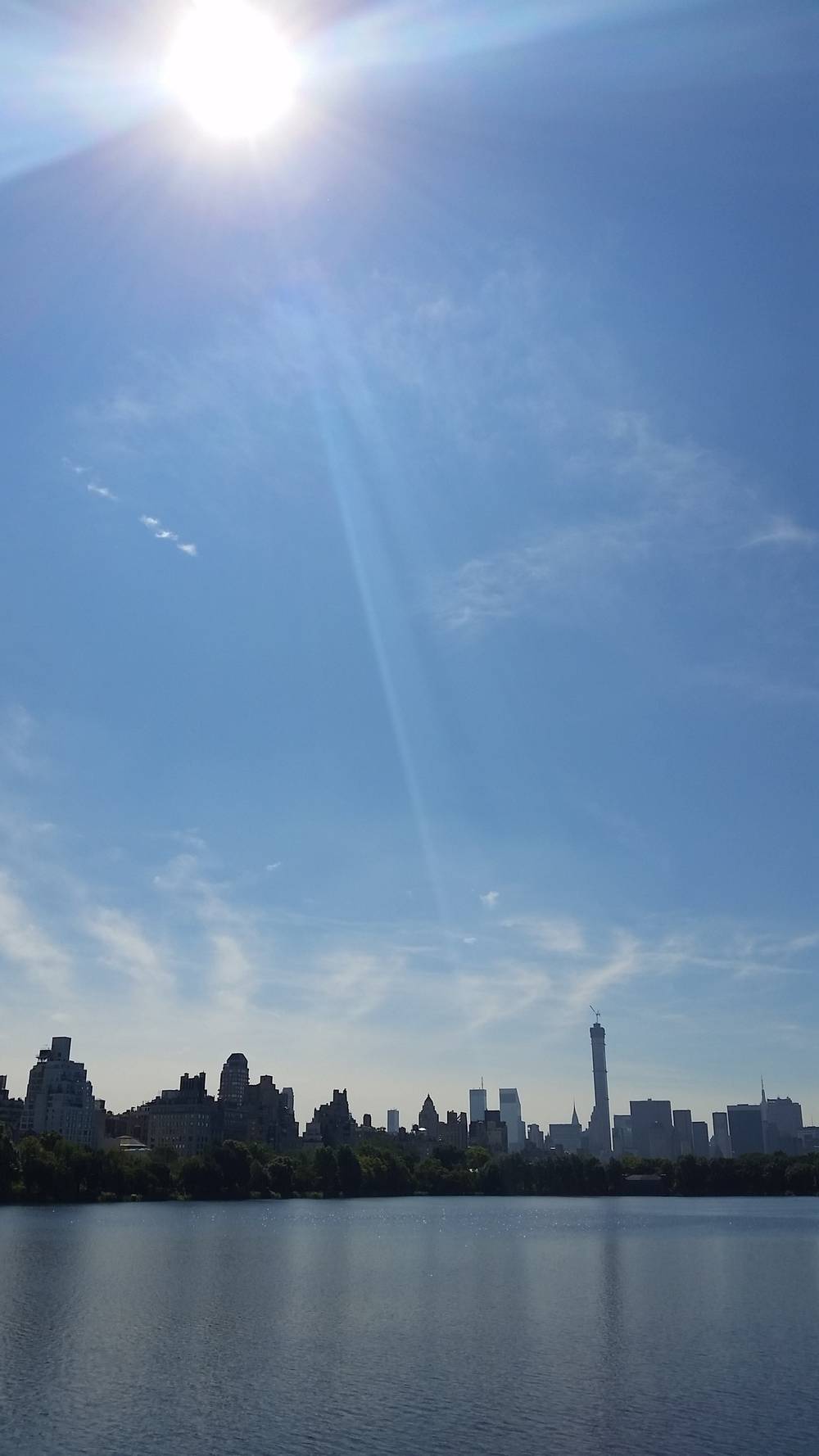 Sunlight beams over the Central Park reservoir with the Manhattan skyline in the distance.