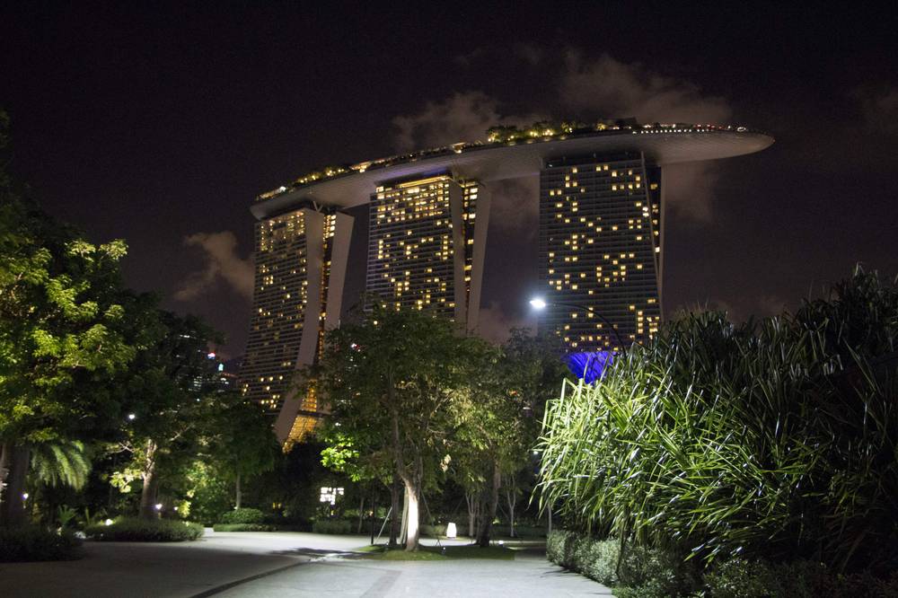 Marina Bay Sands' three towers glow at night above a landscaped garden path.