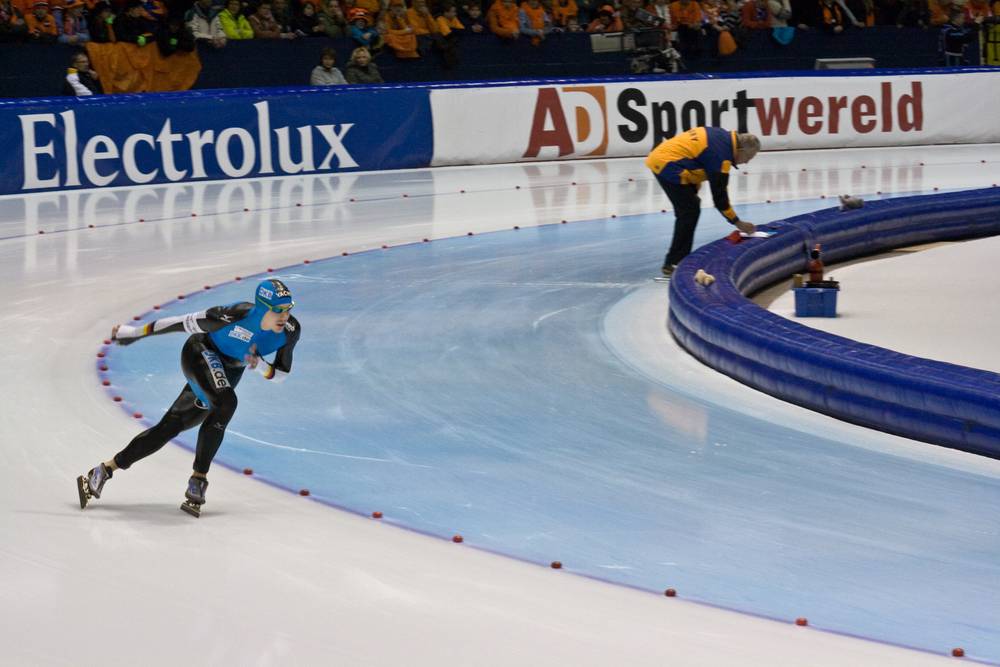 A speed skater races around the curve while an official stands at the rink center.