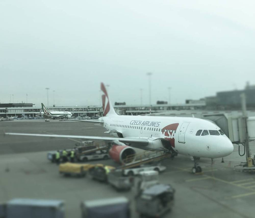 A Czech Airlines jet parked at an airport gate with ground crew and luggage carts nearby.