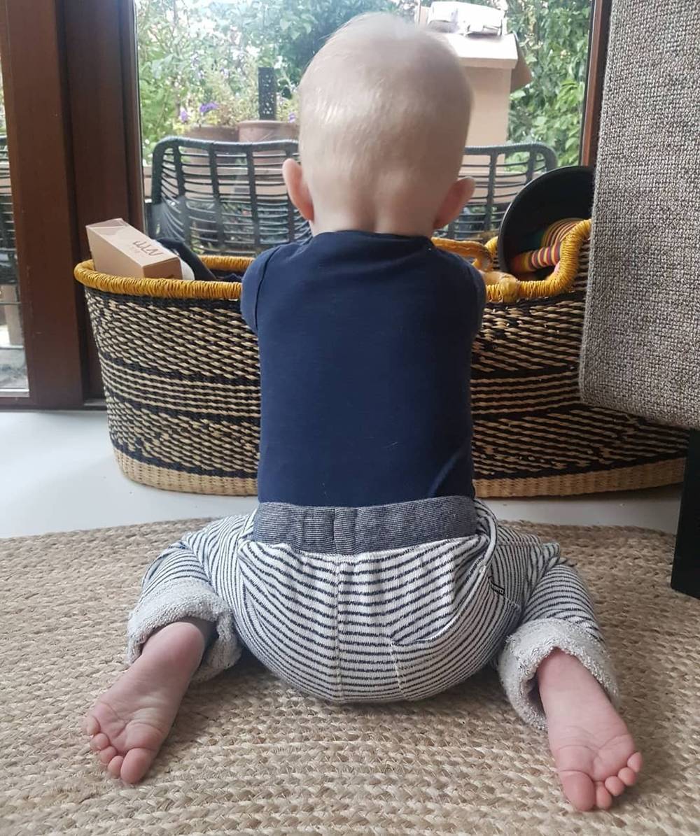 A baby sits on a rug seen from behind, near a woven basket.