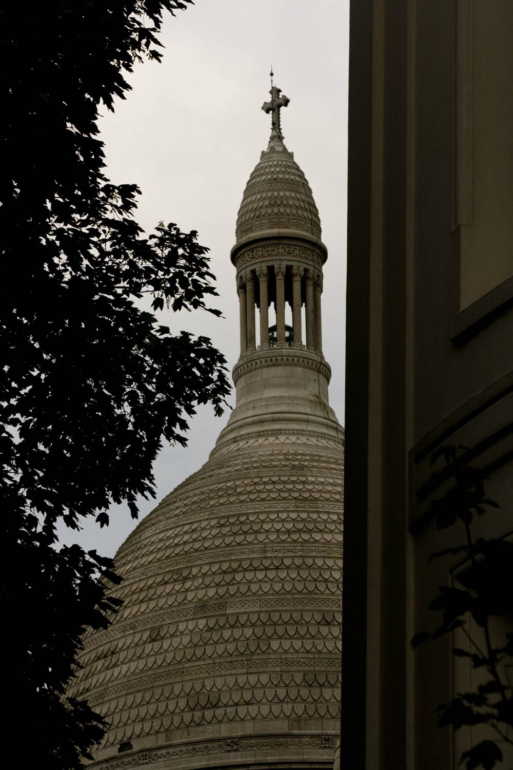 The domed spire of Sacre-Coeur is glimpsed between trees and a building's edge.