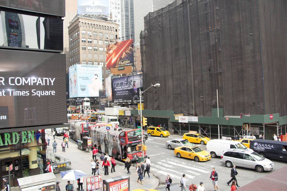 Traffic and pedestrians fill a Times Square intersection beneath billboards.