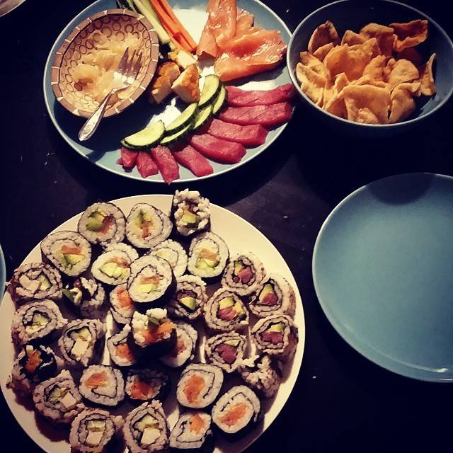 Plates of sushi rolls, sashimi and side dishes arranged on a table.
