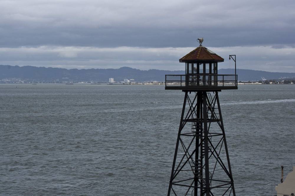 A guard tower stands over the water at the edge of Alcatraz Island.