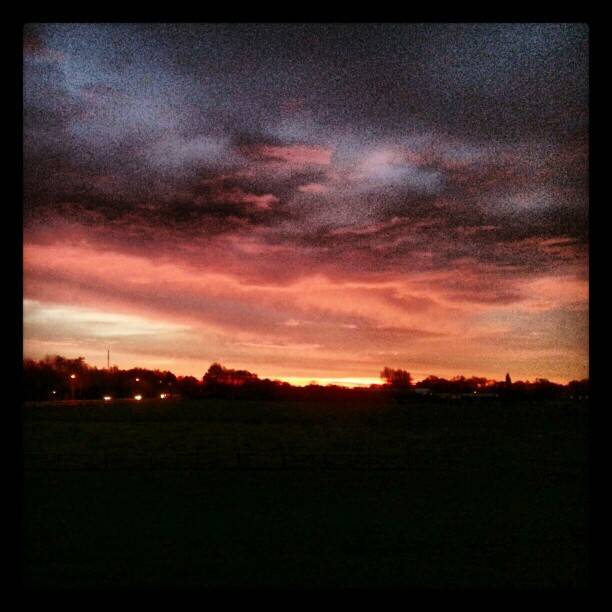 A dramatic pink and orange sunset over a dark field.