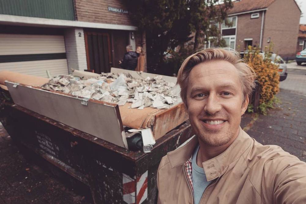 Selfie next to a dumpster filled with renovation debris outside a house.