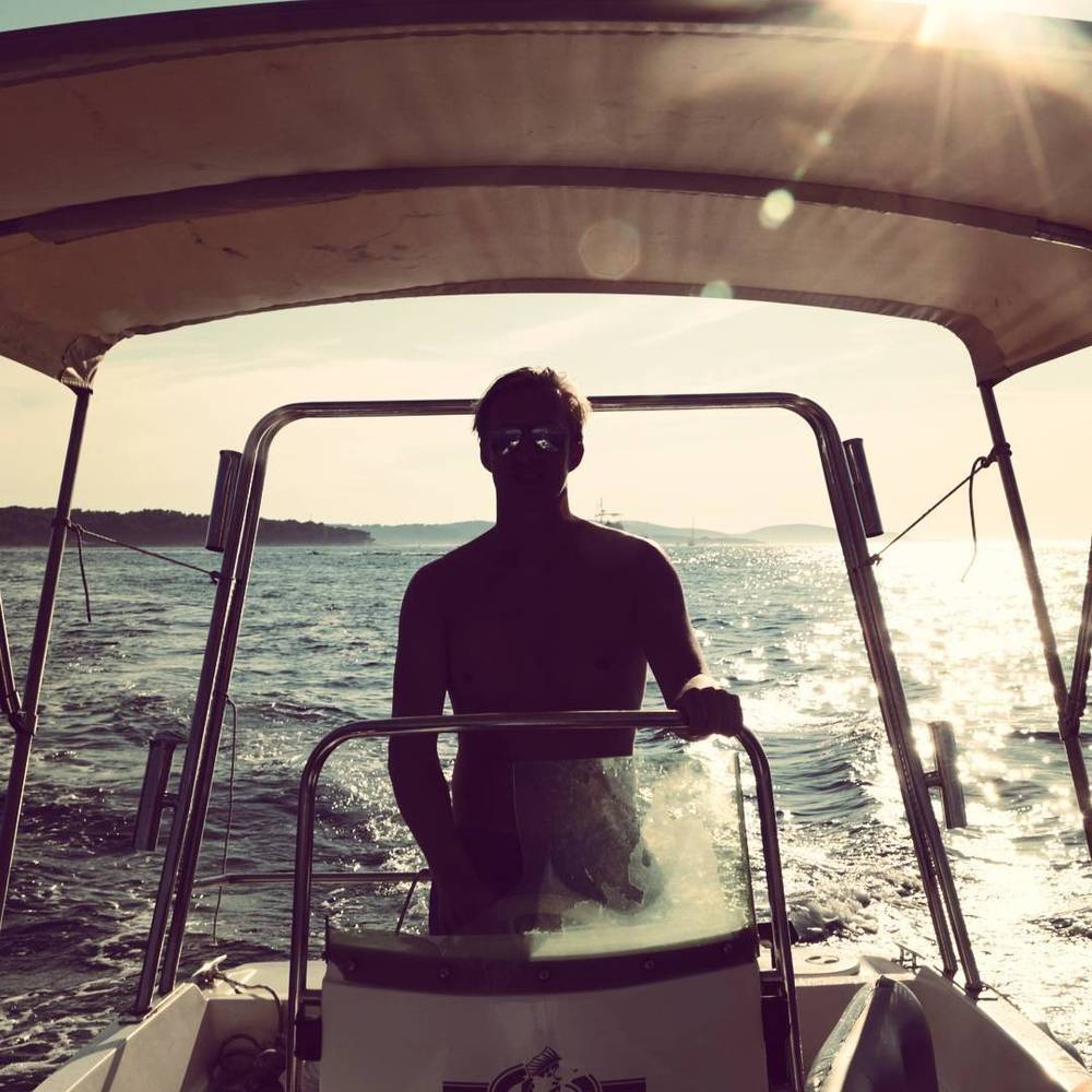 Silhouette of a man steering a boat at sea with sunlight glinting off the water.