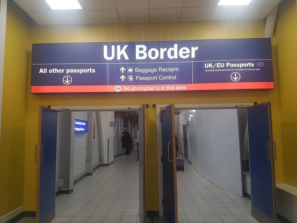 A yellow UK Border sign above open doors leading to passport control.