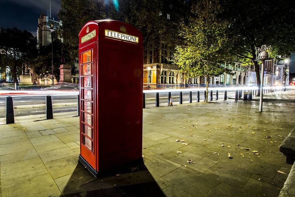 A red telephone box on an empty London street at night.