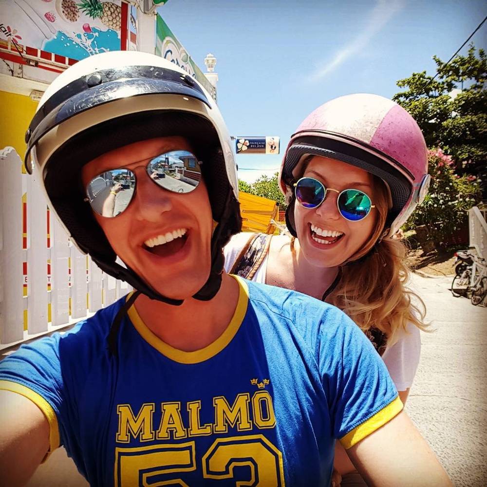 A couple wearing motorcycle helmets and sunglasses smiling for a selfie.