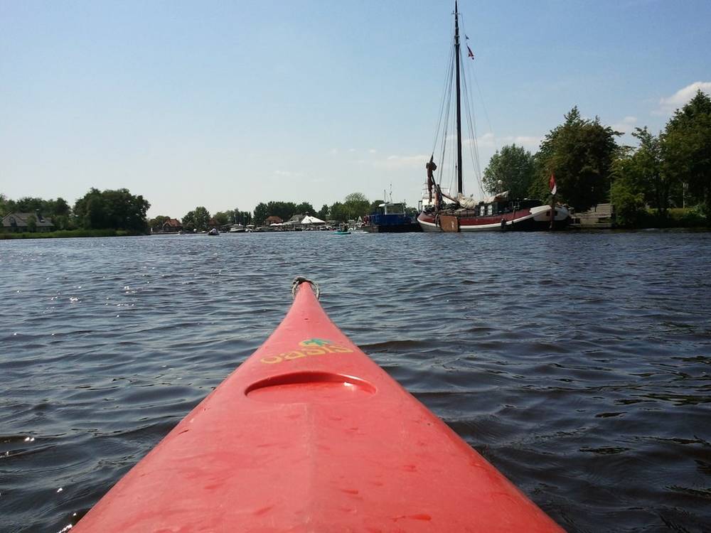 The bow of a red kayak points across calm open water toward moored boats.