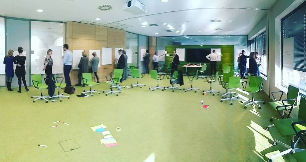 An open-plan office workshop space with green chairs and sticky notes on the floor.
