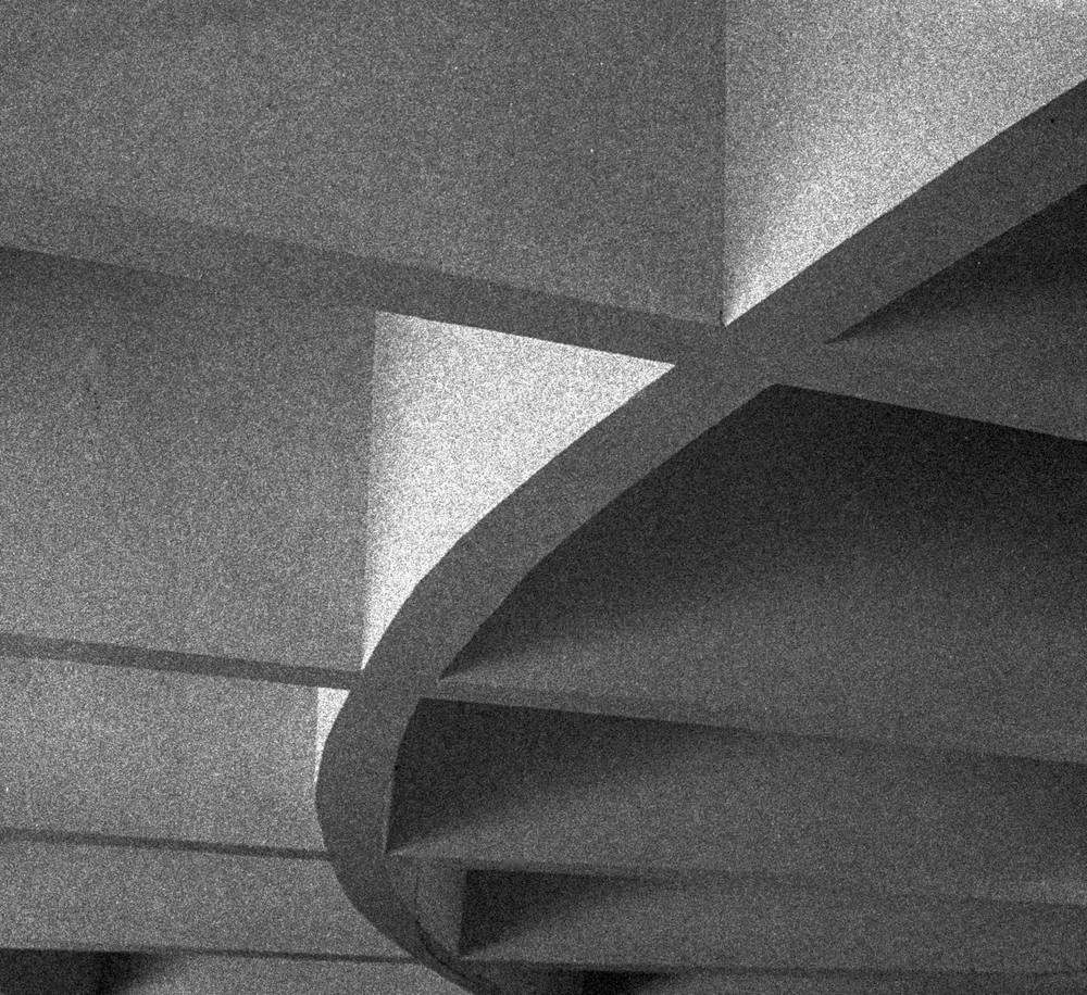 Geometric concrete panels create an abstract pattern of sharp angles and deep shadows in shades of grainy black and white.