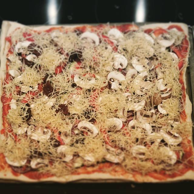 A homemade flatbread pizza topped with cheese, mushrooms and sprouts.