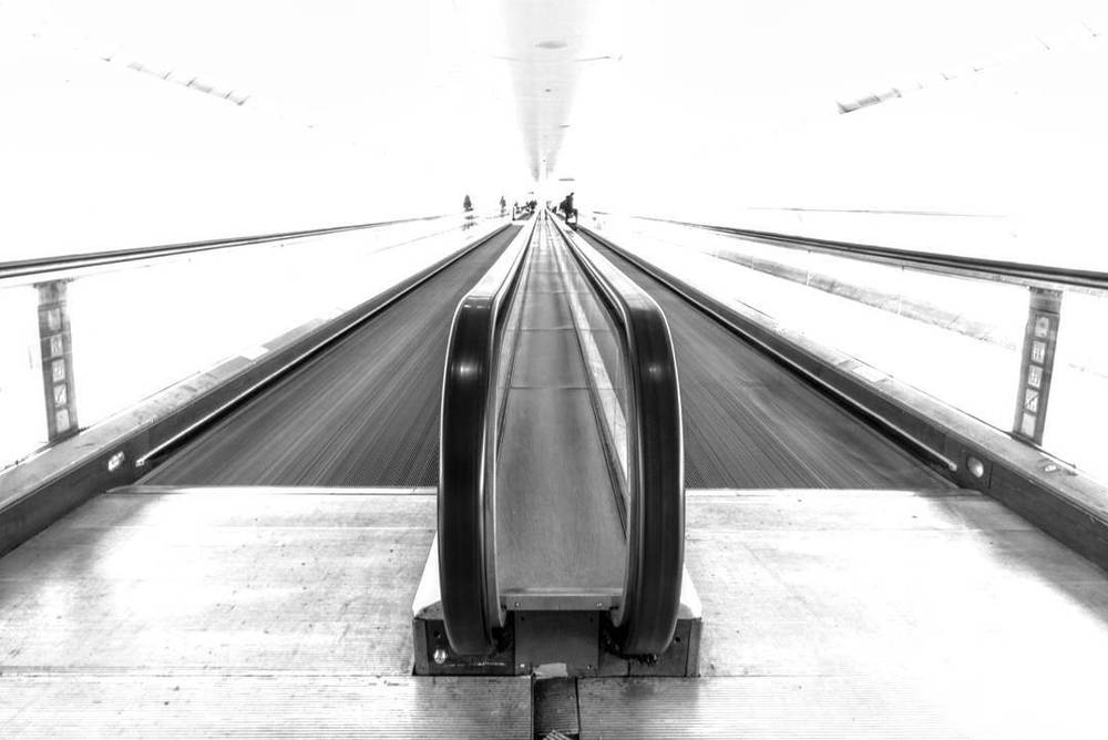 Black and white photo looking down a long escalator and staircase inside a modern building.