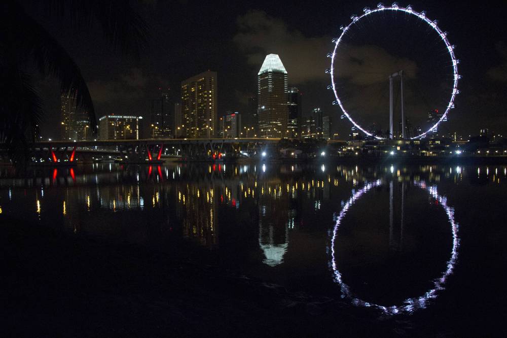 The Singapore Flyer and city skyline reflect in the water at night.