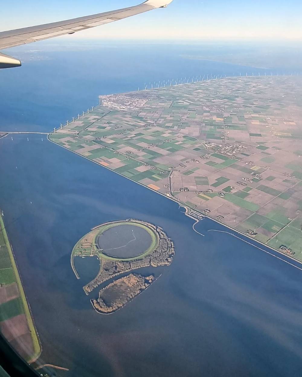 An aerial view from a plane of a coastline with wind turbines and farmland.