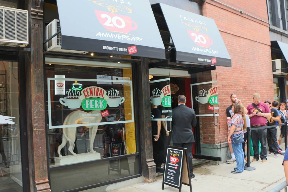 The Central Perk storefront window displays the Friends dog statue and 20th anniversary signage.