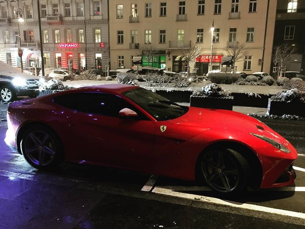 A red Ferrari sports car parked on a snowy city street at night.