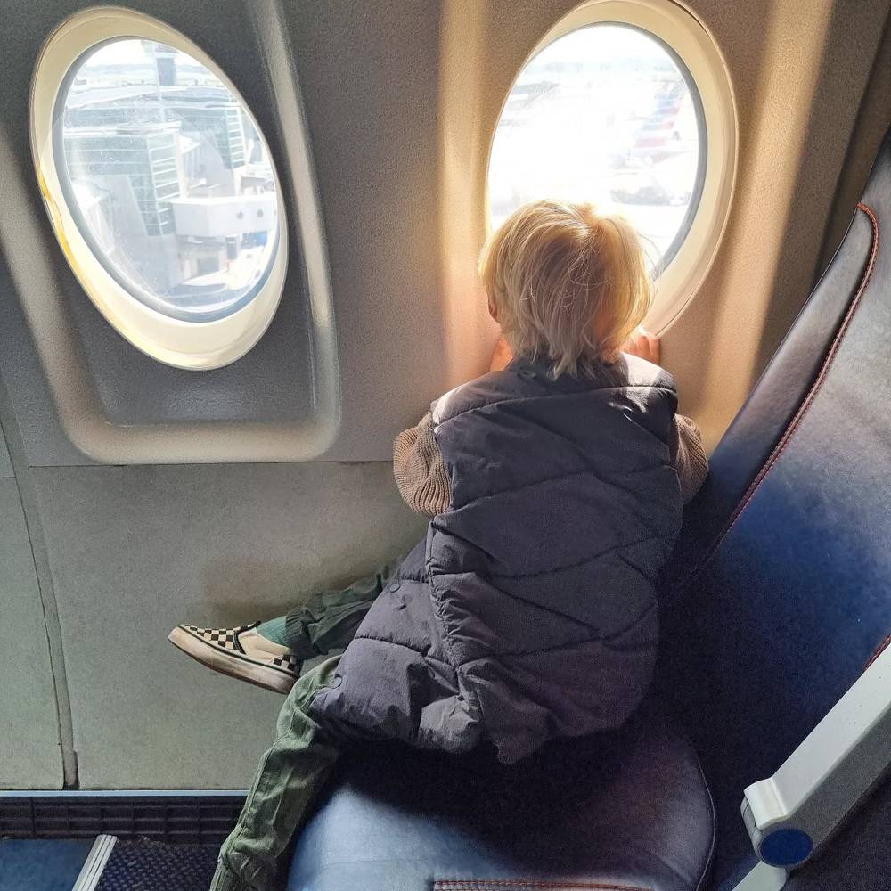 A child sitting in an airplane seat looking out the round window.