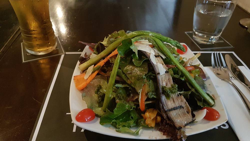 A plate of grilled vegetable salad with cherry tomatoes sits on a restaurant table.