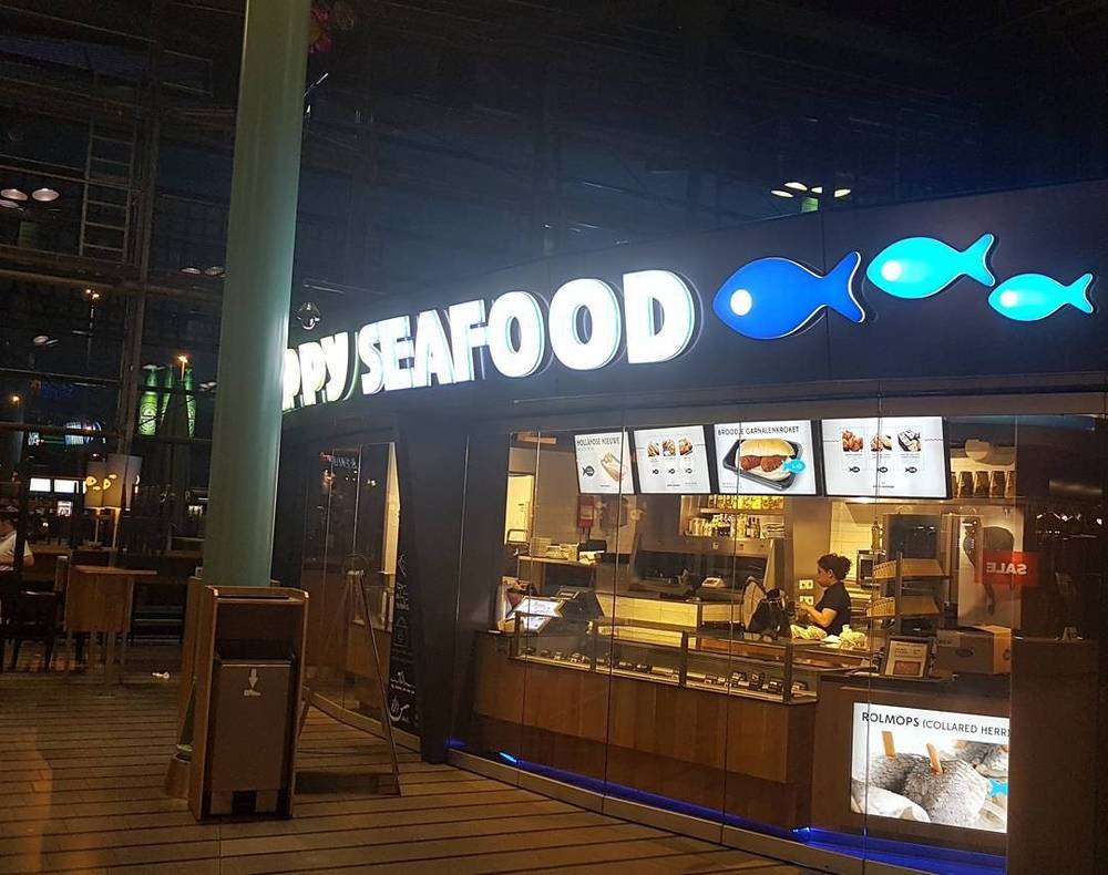 A fast-food seafood counter called "Happy Seafood" with a menu board and staff preparing food.